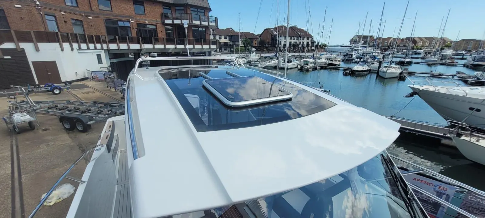 A view of a boat's roof with a skylight, overlooking a marina filled with moored yachts and clear blue skies.